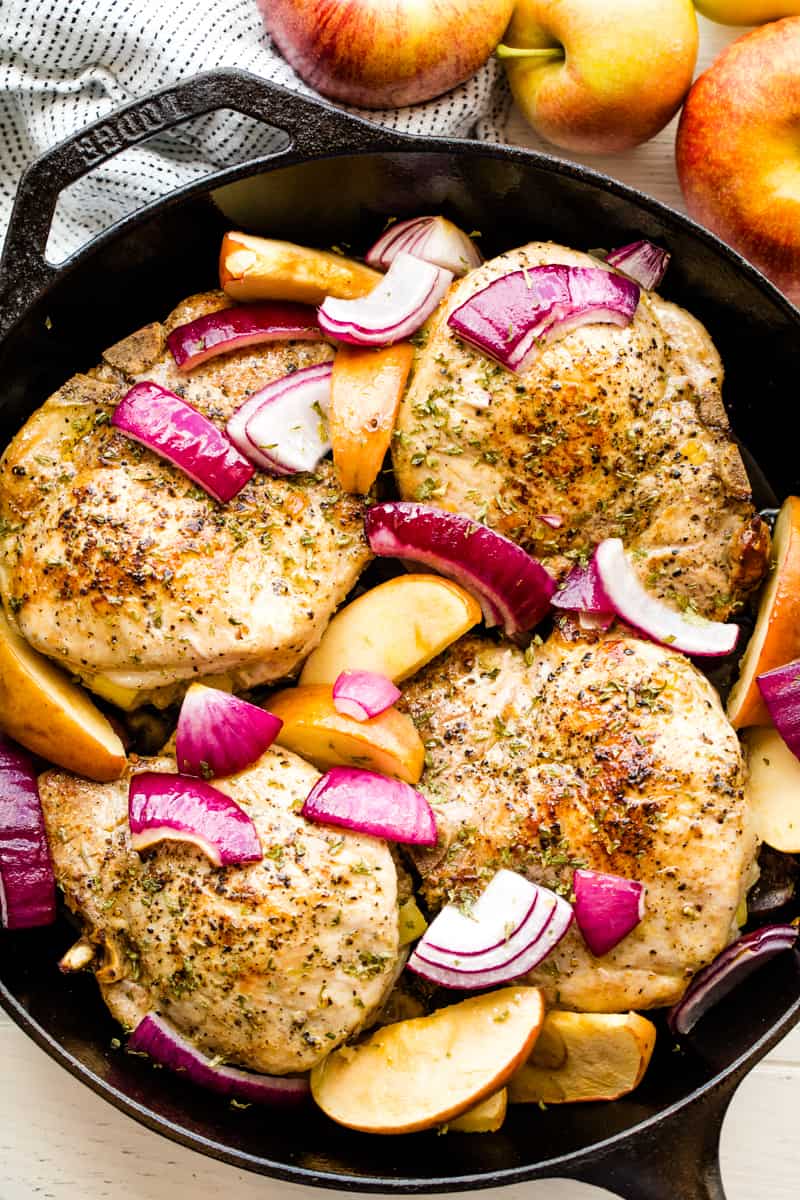 A skillet full of Apple Stuffed Pork Chops slightly covered by onion slices and apple wedges.