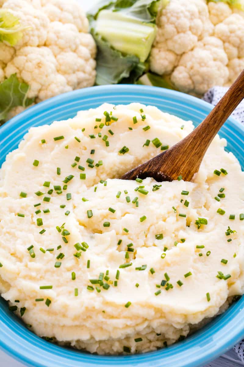 Mashed Cauliflower in a blue bowl with a wooden spoon in it.