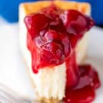 Close up of a slice of New York Cheesecake topped a cherry topping with a bite taken out of it on a white plate.