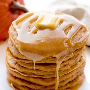 A stack of pumpkin pancakes topped with a pad of butter and syrup.