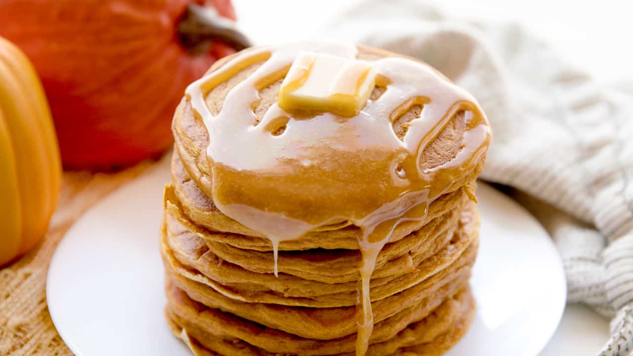 A stack of pumpkin pancakes topped with a pad of butter and syrup.