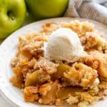 Served up apple cobbler on a white plate with a scoop of ice cream on it.