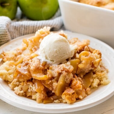 Apple cobbler served up of a white plate topped with a scoop of icecream.