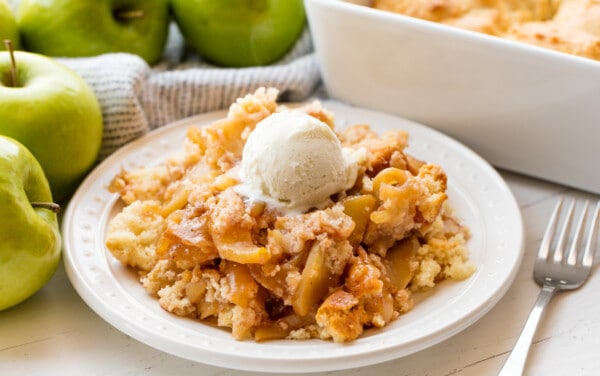 Apple cobbler served up of a white plate topped with a scoop of icecream.