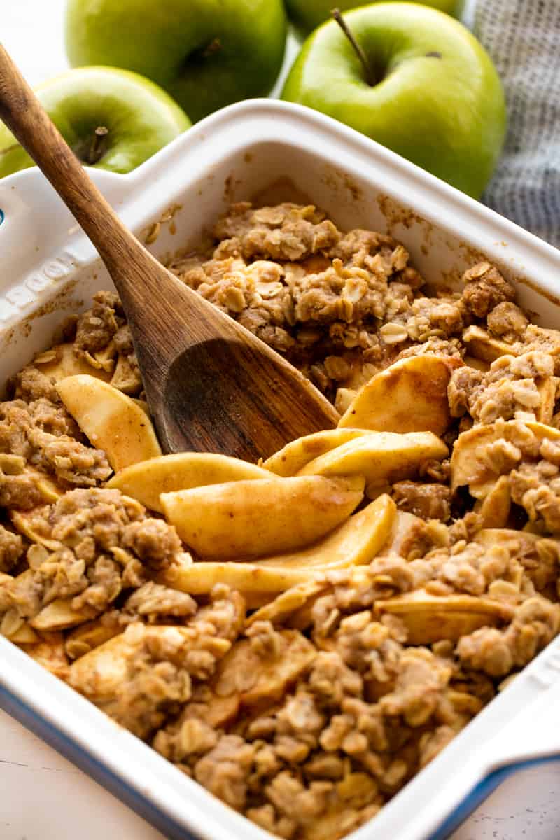 Apple Crisp in a baking dish with a wooden spoon in it.