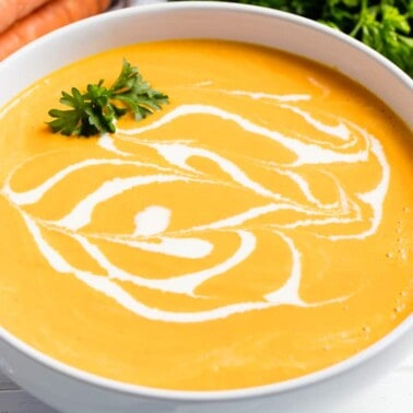 Carrot soup drizzled with cream and garnished with parsley in a white bowl
