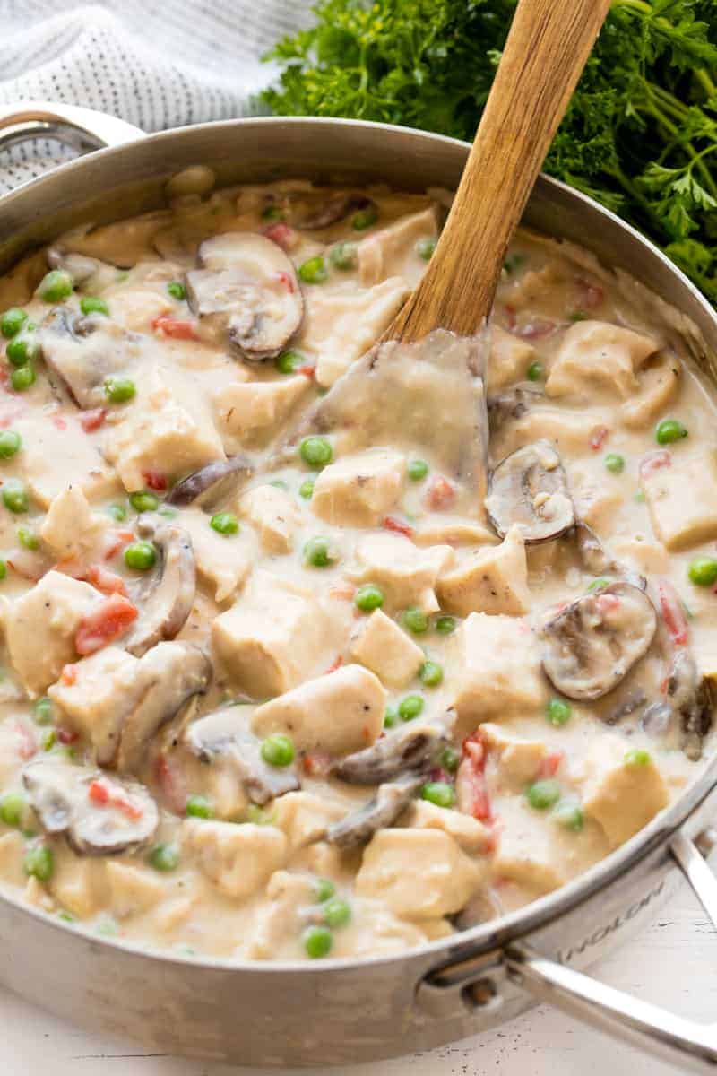 Chicken a la King in a pan getting stirred by a wooden spoon.