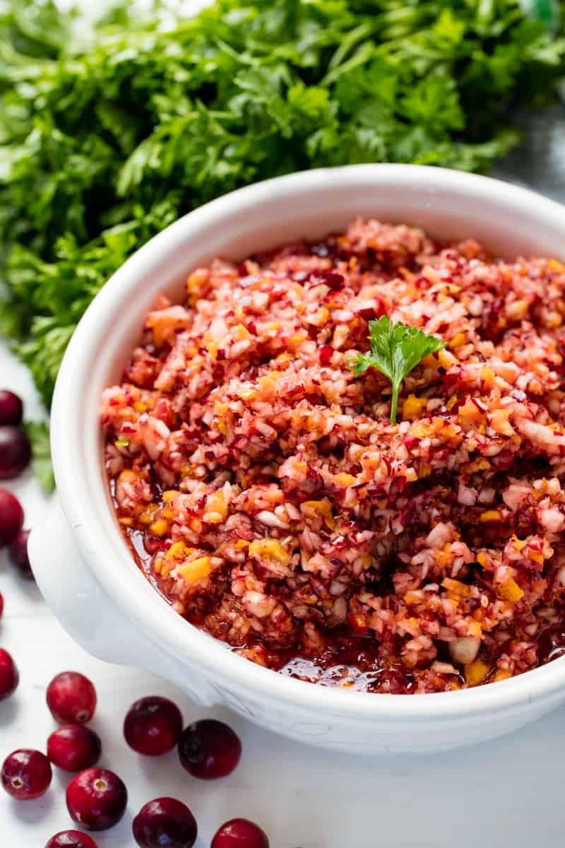 Cranberry Relish in a white bowl topped with a leaf of parsely..