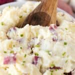 Garlic Mashed Potatoes in a white bowl with a wooden spoon in it.