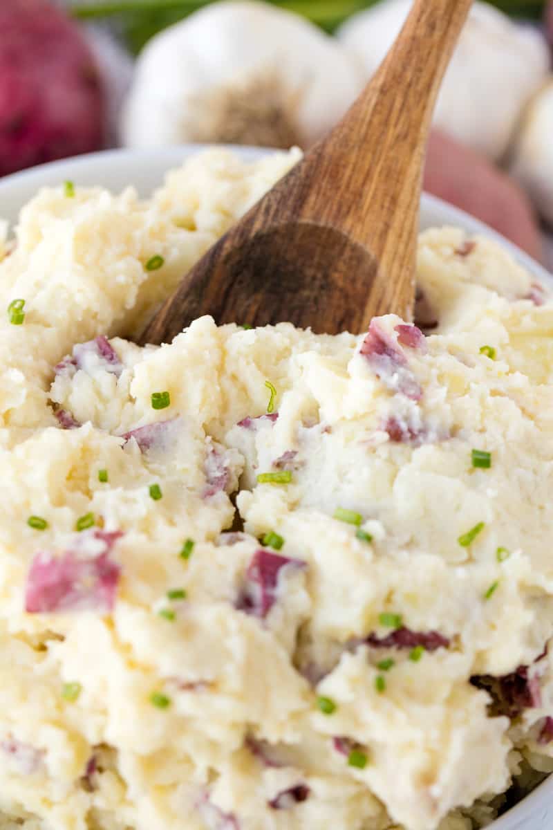 Garlic Mashed Potatoes in a white bowl with a wooden spoon in it.