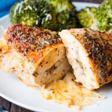 Stuffed chicken breasts cut in half with the cheese oozing out on a white plate.