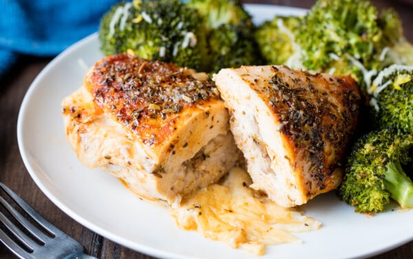 Stuffed chicken breasts cut in half with the cheese oozing out on a white plate.