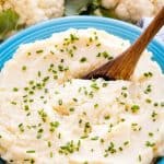 Mashed Cauliflower in a blue bowl with a wooden spoon in it.