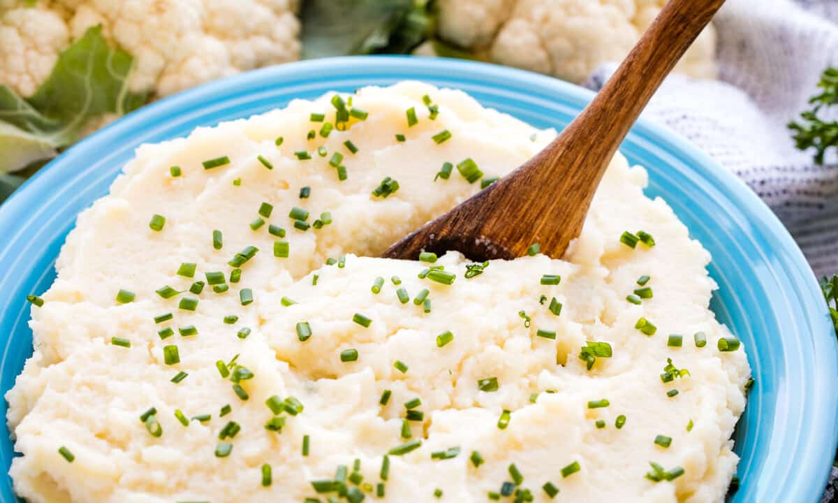 Mashed cauliflower in a blue bowl with a wooden spoon in it.