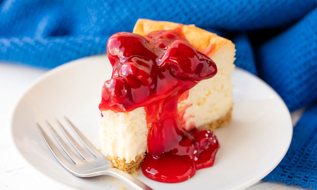 A slice of cheesecake with a bite taken out of it topped with cherries and a cherry sauce on a white plate.
