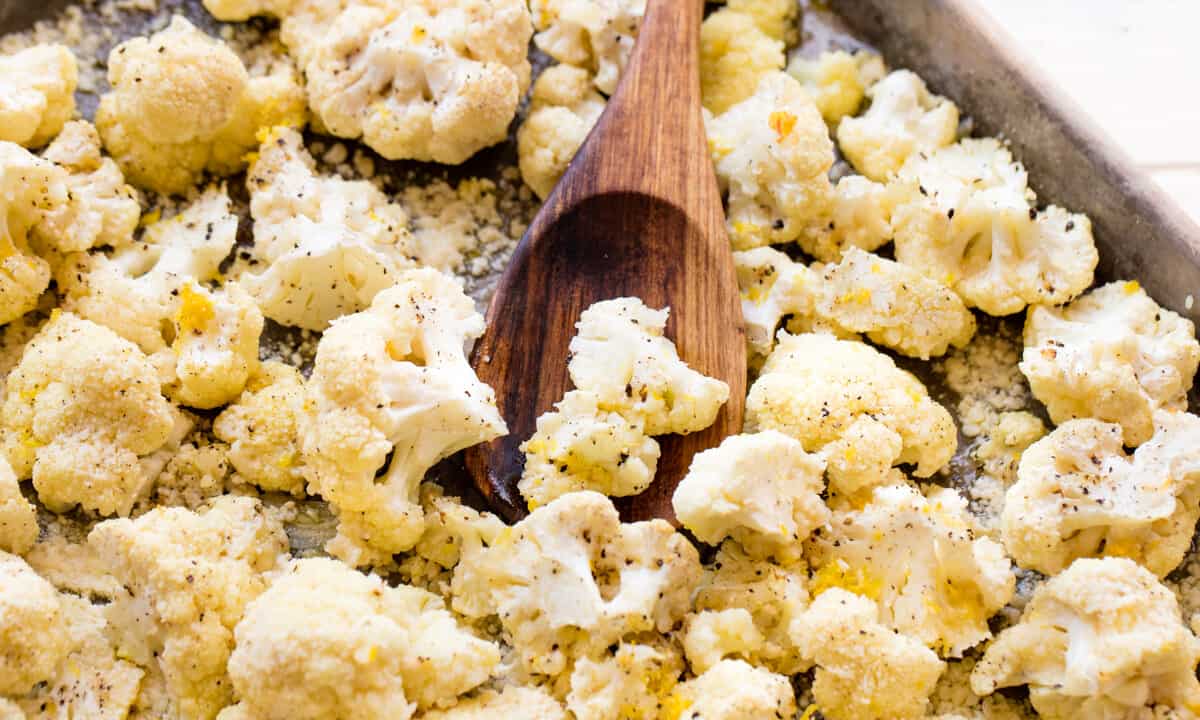 Close up of roasted cauliflower on a pan with a wooden spoon on it.