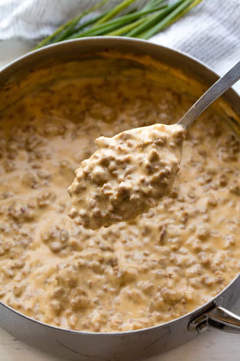 A spoonful of Sausage Gravy over a pan full of sausage gravy.