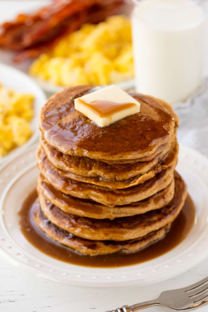 Whole Wheat Pancakes stacked up on a white plate topped with a pad of butter and syrup.