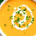 Sweet Potato Soup in a white bowl topped with cream and green onions.