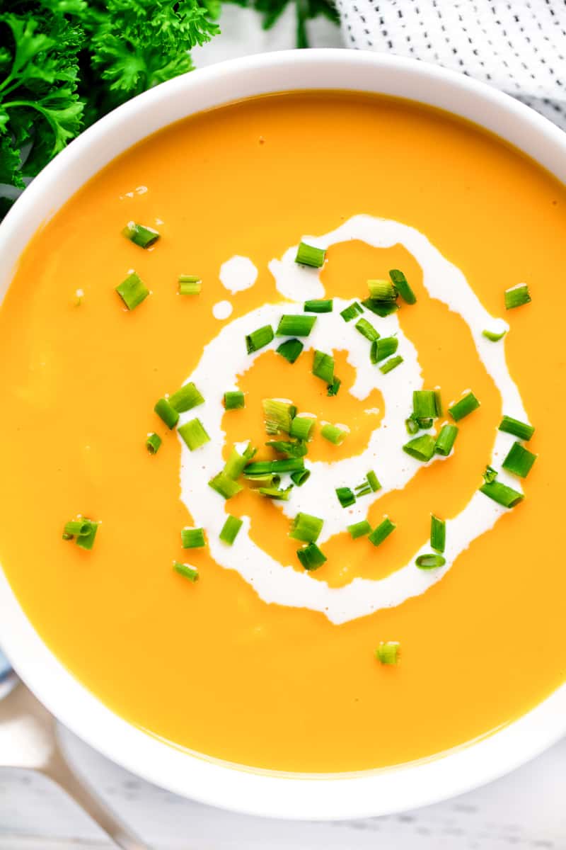 Sweet Potato Soup in a white bowl topped with cream and green onions.