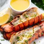 Broiled Lobster Tails on a white plate with a small bowl of butter.