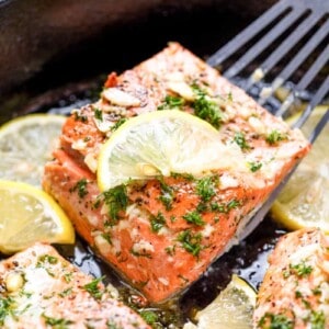 Salmon being lifted out of a skillet with a spatula.