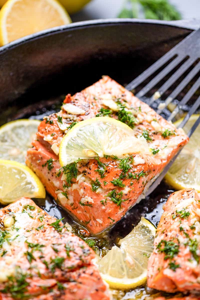 Salmon being lifted out of a skillet with a spatula. 