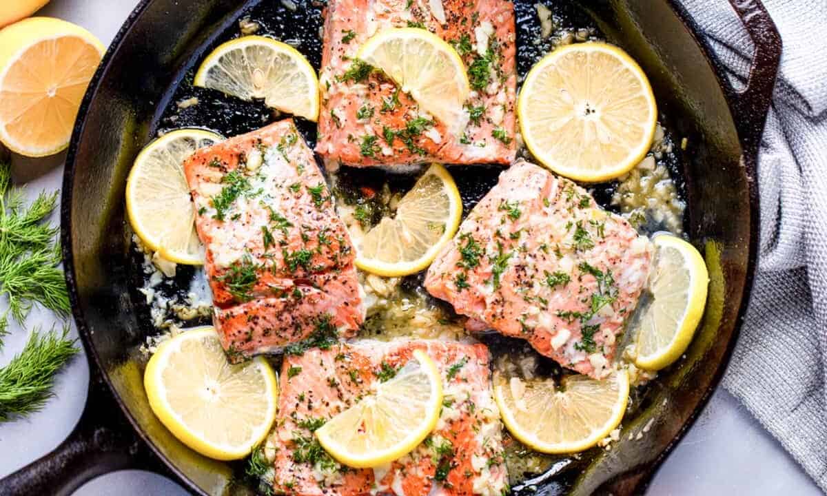 Overhead view of Salmon in a skillet surrounded by lemon slices.