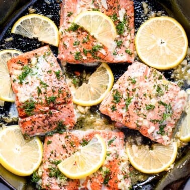 Overhead view of Salmon in a skillet surrounded by lemon slices.