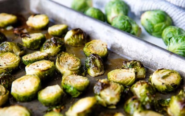 Roasted Brussel Sprouts on a baking sheet with raw sprouts in the background.