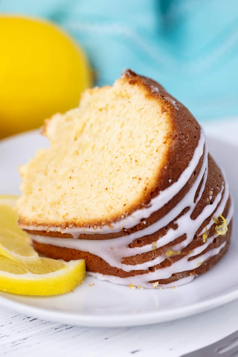 A slice of lemon pound cake on a white plate with a slice of lemon.