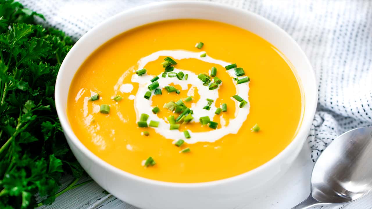 Sweet Potato Soup in a white bowl topped with cream and green onions.