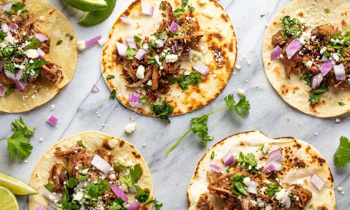 Bird's eye view of Beer Braised Carnitas on top of flour tortilla shells with red onion and cilantro.