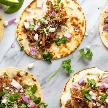 Bird's eye view of Beer Braised Carnitas on top of flour tortilla shells with red onion and cilantro.