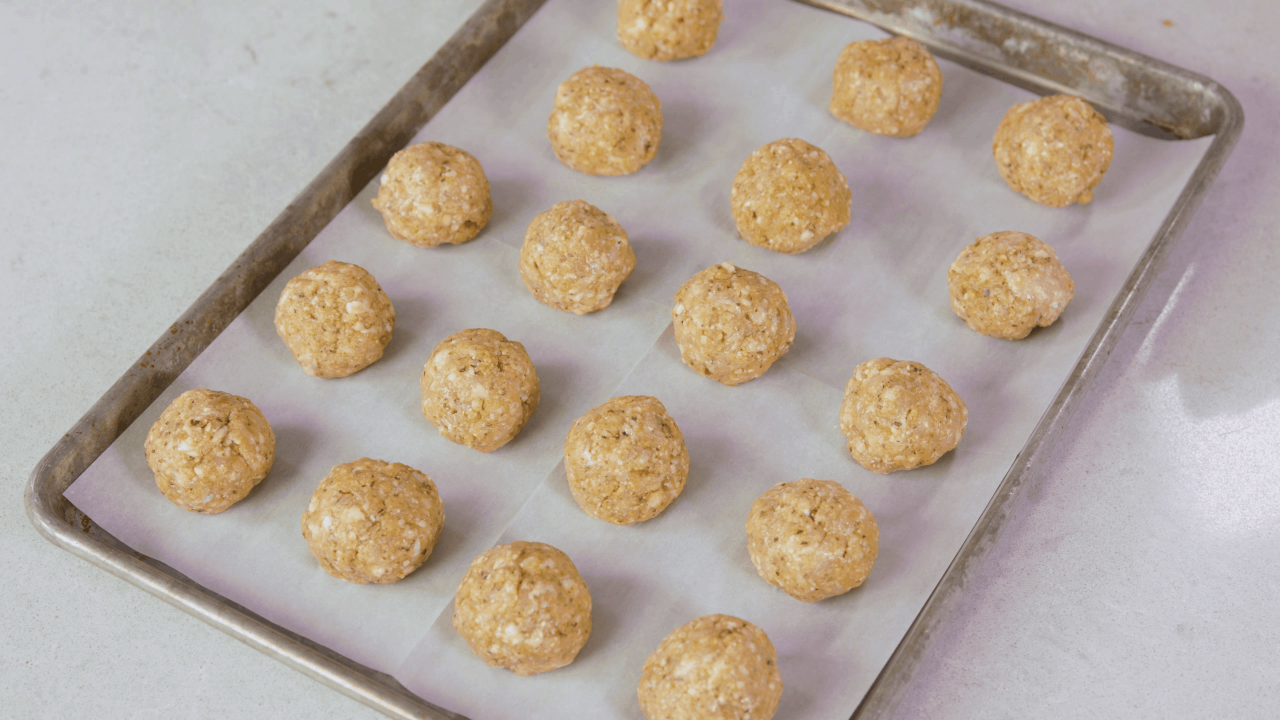  Raw chicken meatballs laying on a parchment paper-covered baking sheet.