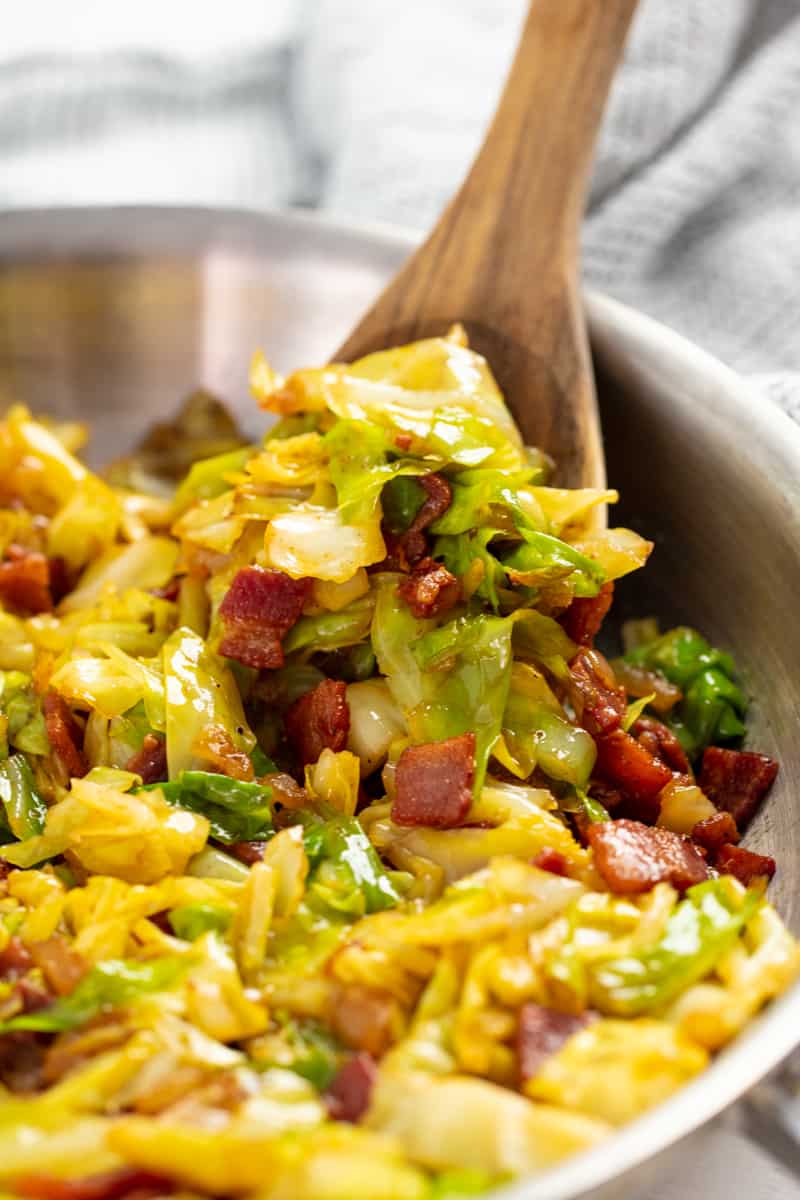 Fried Cabbage in a stainless steel pan with a wooden spoon in it.