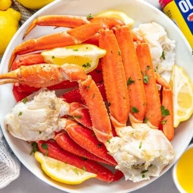Cooked Crab Legs topped with some lemon wedges on a white plate.