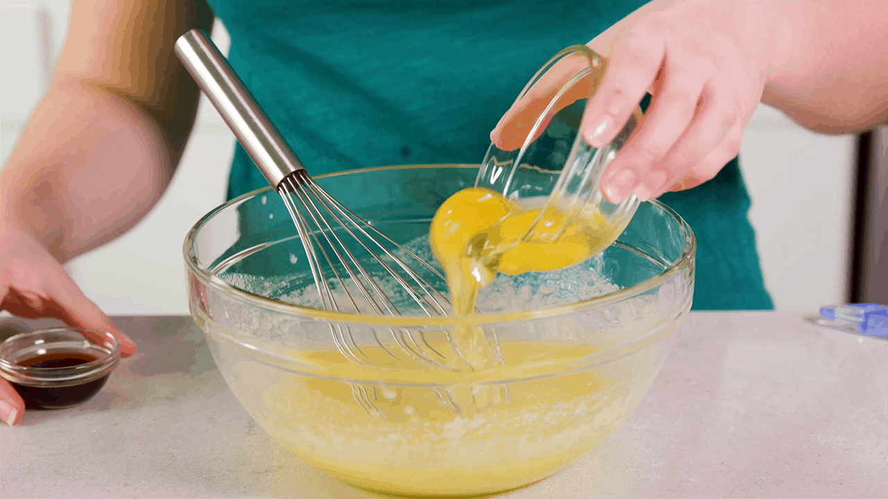 Adding eggs to a mixing bowl with creamed butter and sugar