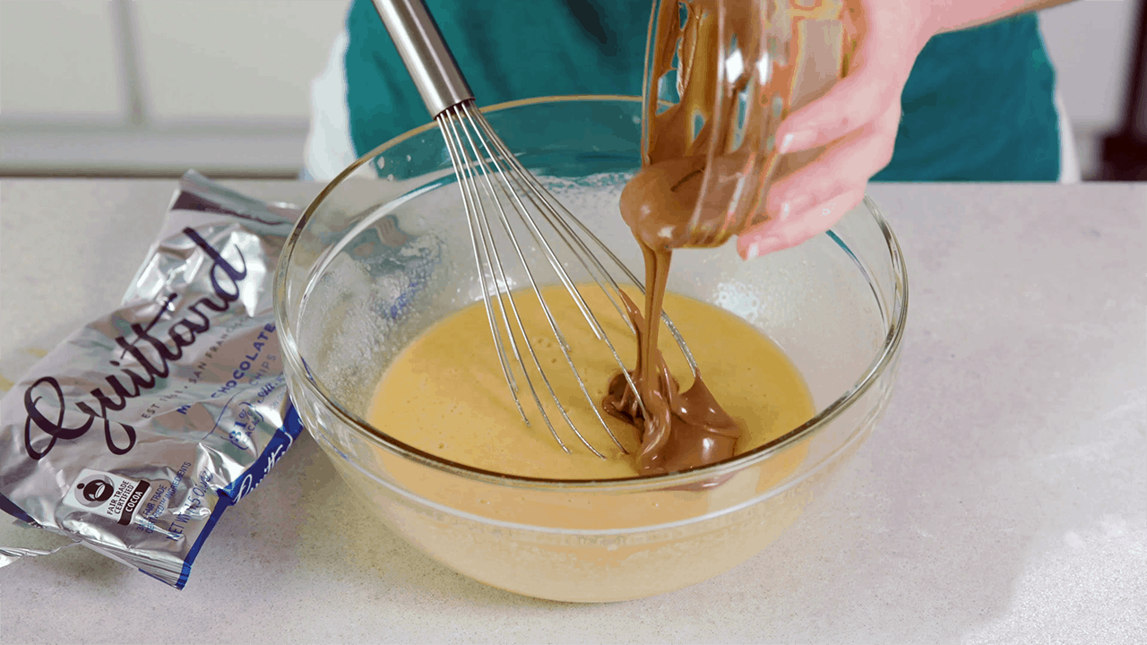 Melted chocolate being scraped into a mixing bowl with other ingredients