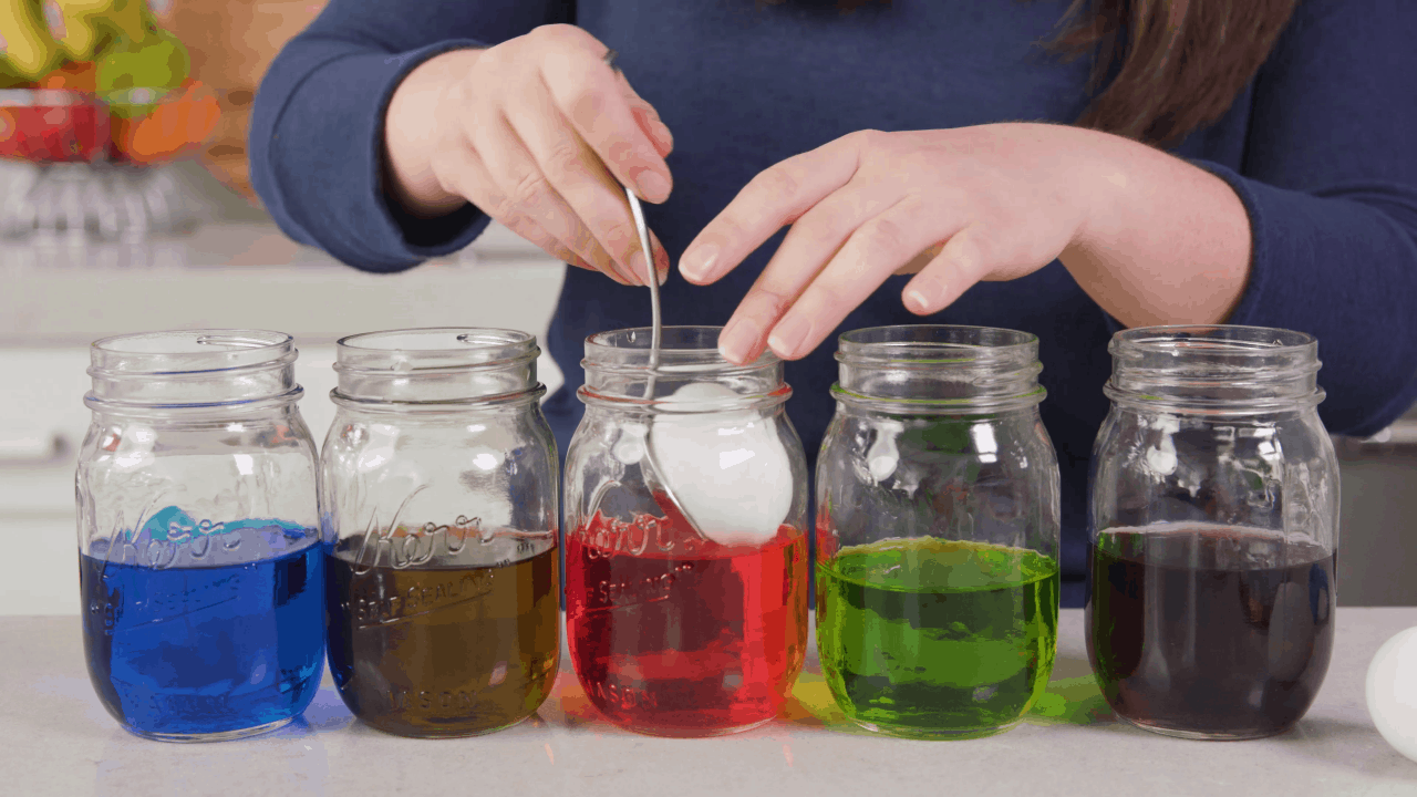 Five mason jars full of food color with the red one getting an egg placed in it. Food Coloring