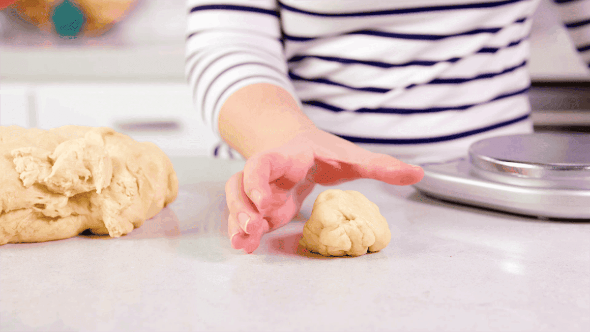 Hand in cupping shape with a piece of roll dough ready to be shaped.