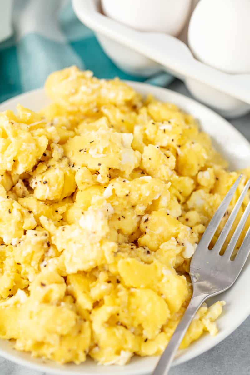 Close up of scrambled eggs on a white plate with a fork on it.