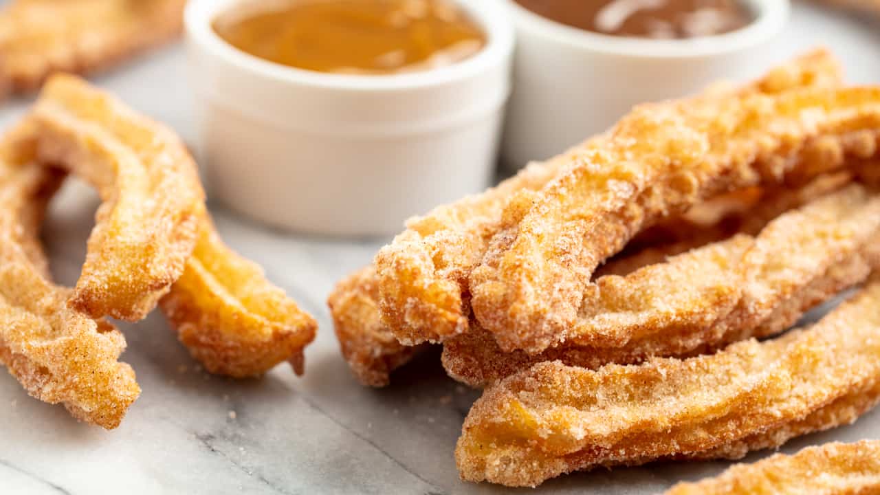 Angled view of Churros on a marble countertop with a bowl of caramel sauce and a bowl of chocolate sauce.