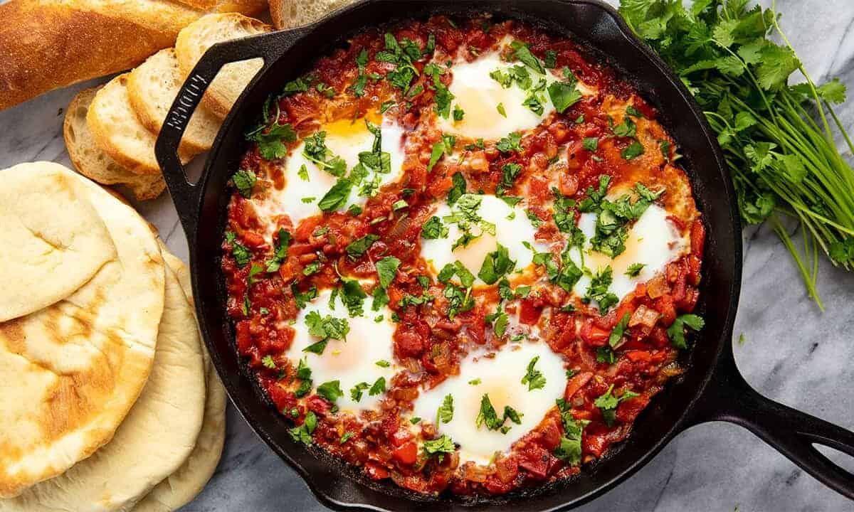 Bird's eye view of Shakshuka in a cast iron skillet surrounded by pita bread.