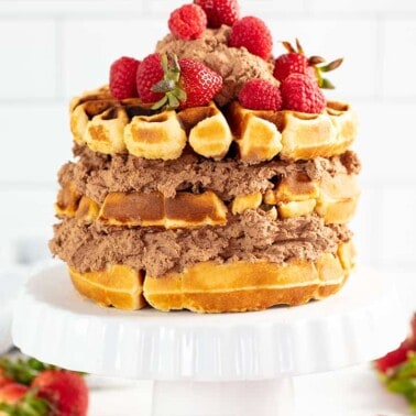 Waffle Cake on a cake stand surrounded by strawberries.