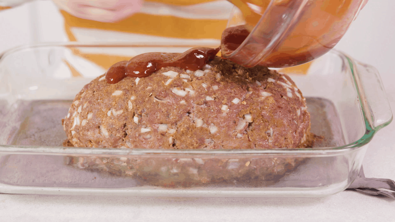 Glaze being poured over a shaped meatloaf in a glass baking dish