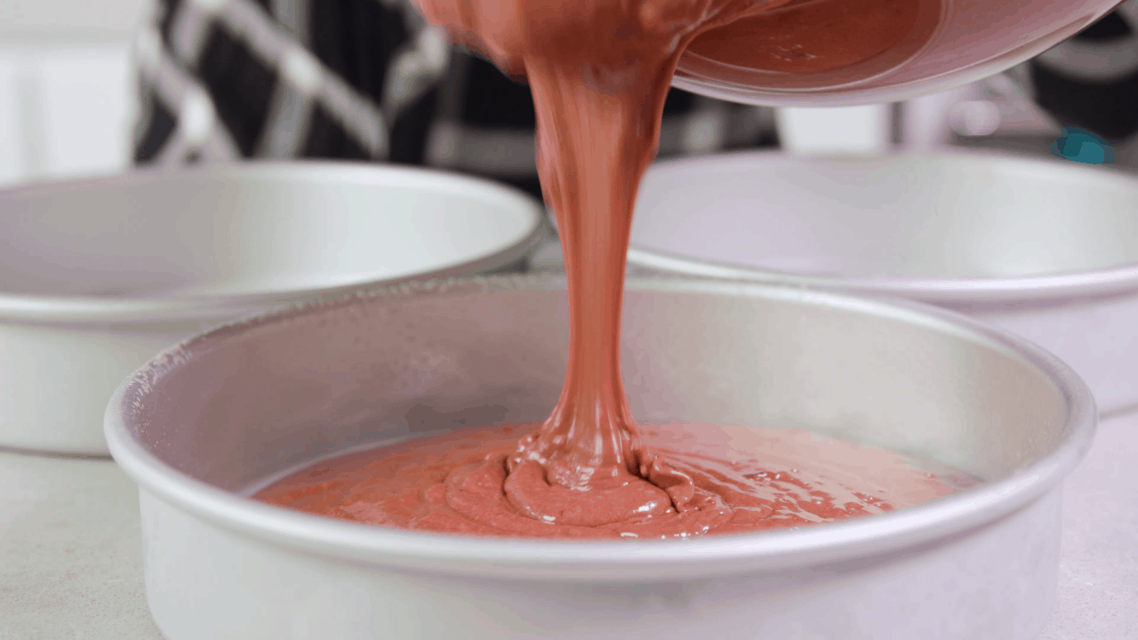 Red Velvet Cake Batter being placed into three cake pans.