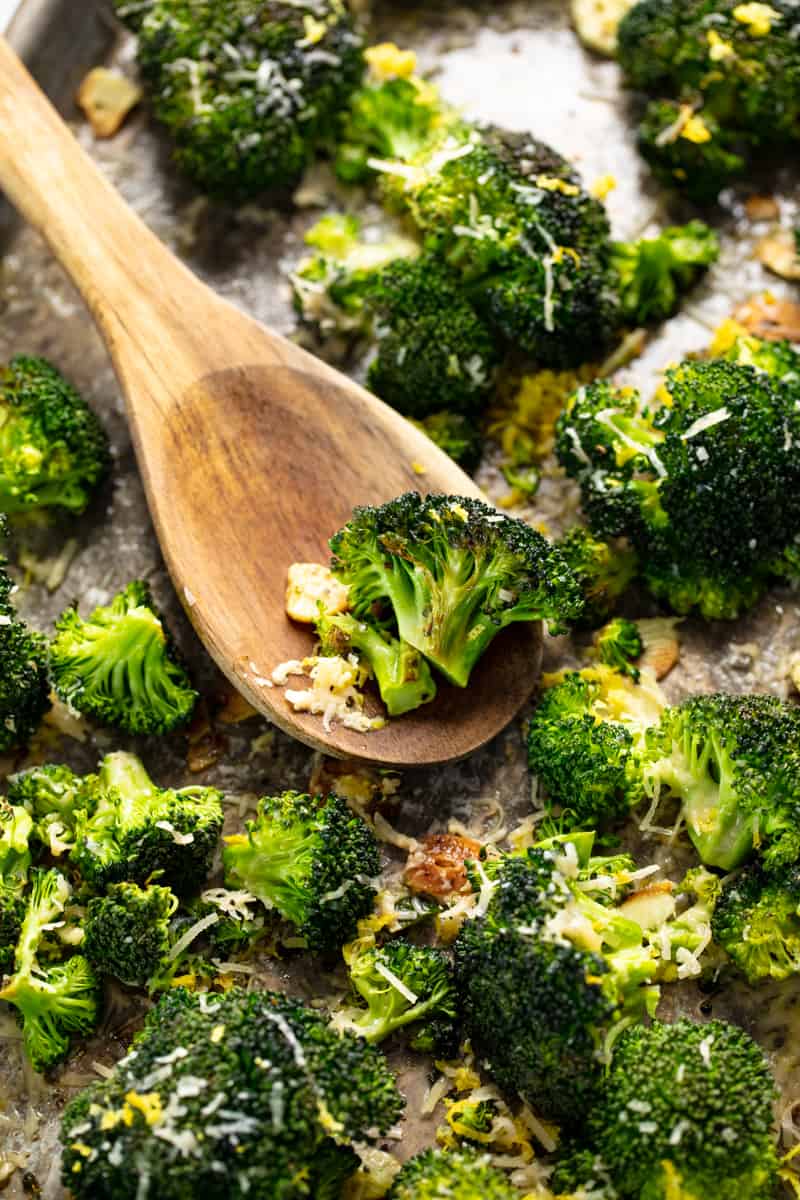 Roasted Broccoli on a baking sheet with some broccoli on a wooden spoon on the baking sheet.