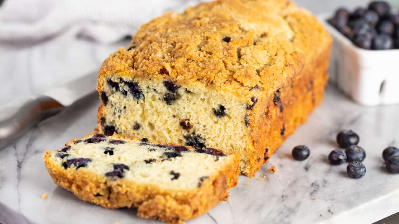 Loaf of Blueberry Pancake Bread on a marble slab with the end sliced to reveal a cross-section of blueberries inside.
