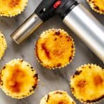Bird's eye view of Creme Brulee Cheesecake Cupcakes and a kitchen torch on a marble countertop.